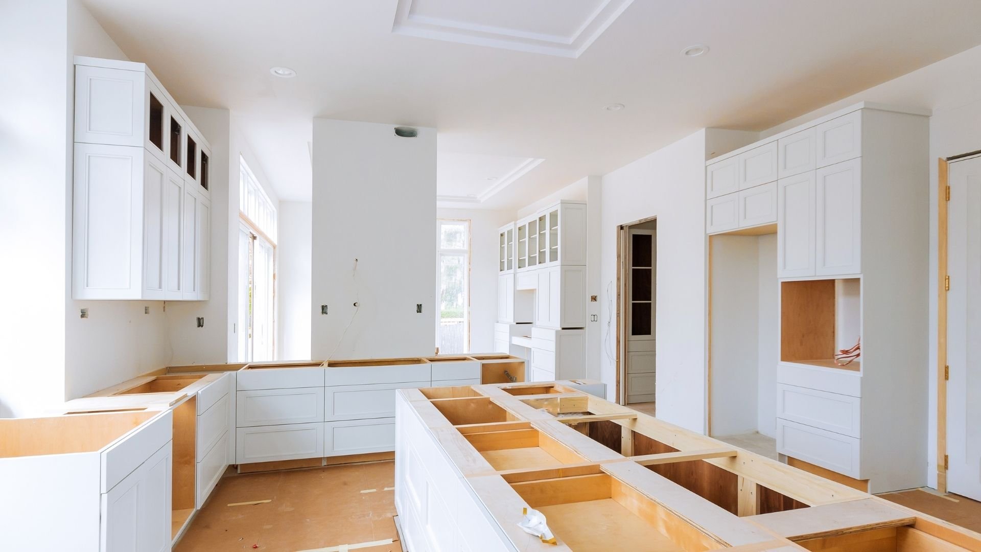 Modern kitchen under construction with white cabinetry and wooden countertop framing exposed.