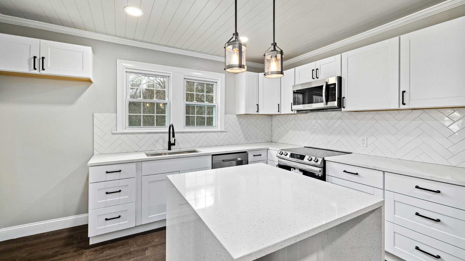Modern white kitchen with island, herringbone backsplash, stainless steel appliances, pendant lights