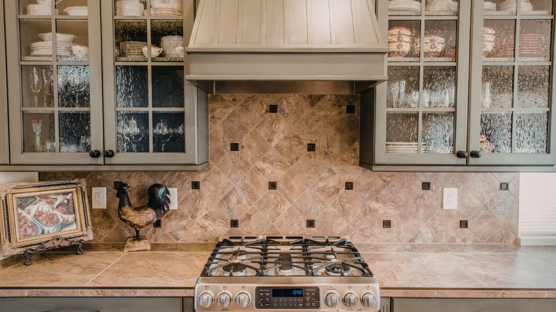 Elegant kitchen with cream cabinets, marble backsplash, gas cooktop, and glass-door cabinetry displaying dishes.