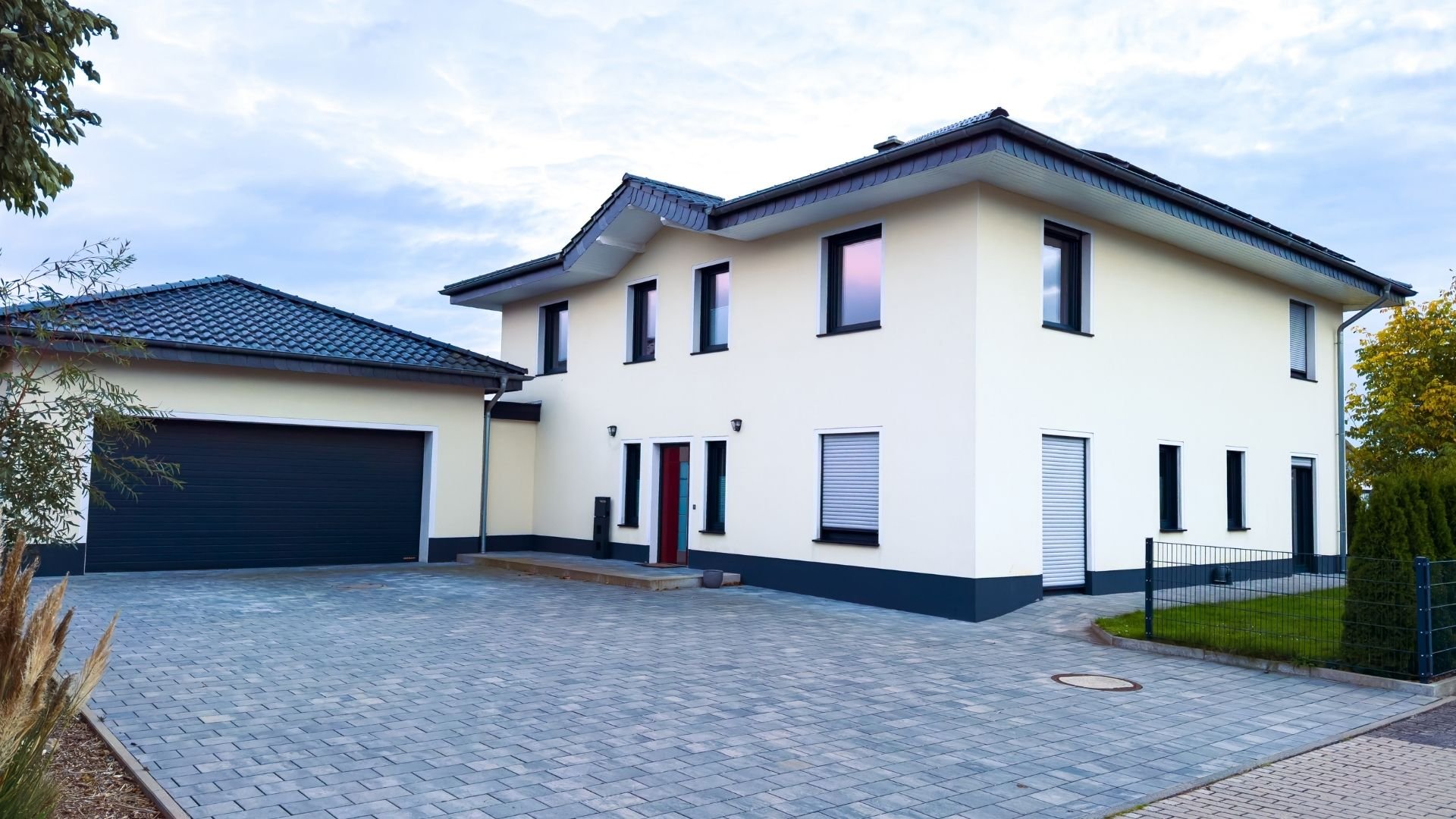 Modern white house with dark roof, garage, red door, and paved driveway
