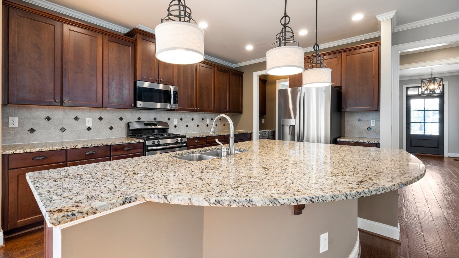 Modern luxury kitchen with granite countertops, wooden cabinets, stainless steel appliances, and pendant lighting.